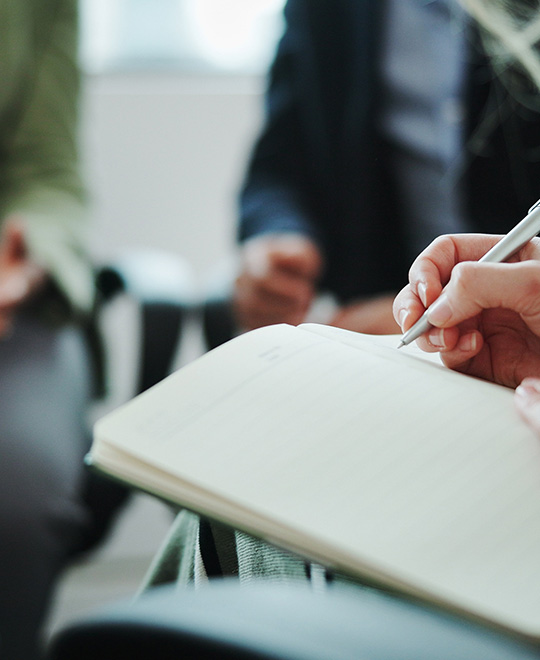 Jemand notiert etwas in seinem Notizbuch uns sitzt dabei in Gruppe von Menschen